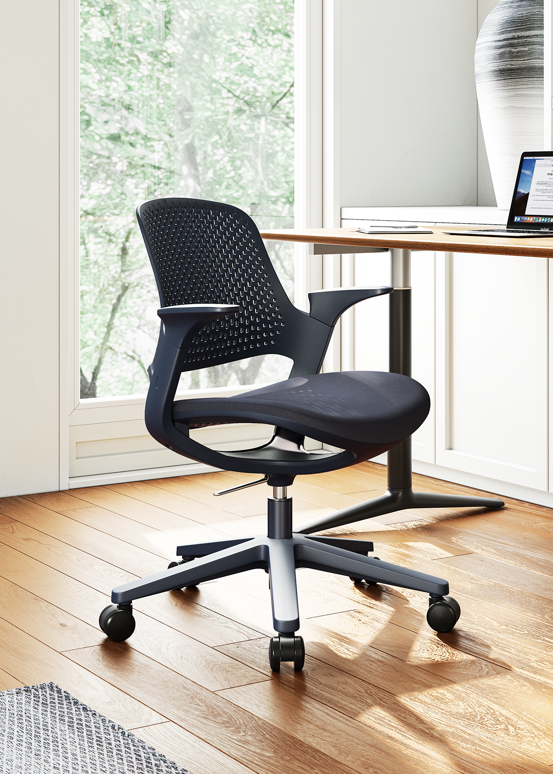 Inke chair with armrests and mesh back on wooden floor near a desk with a laptop and large vase by a window.