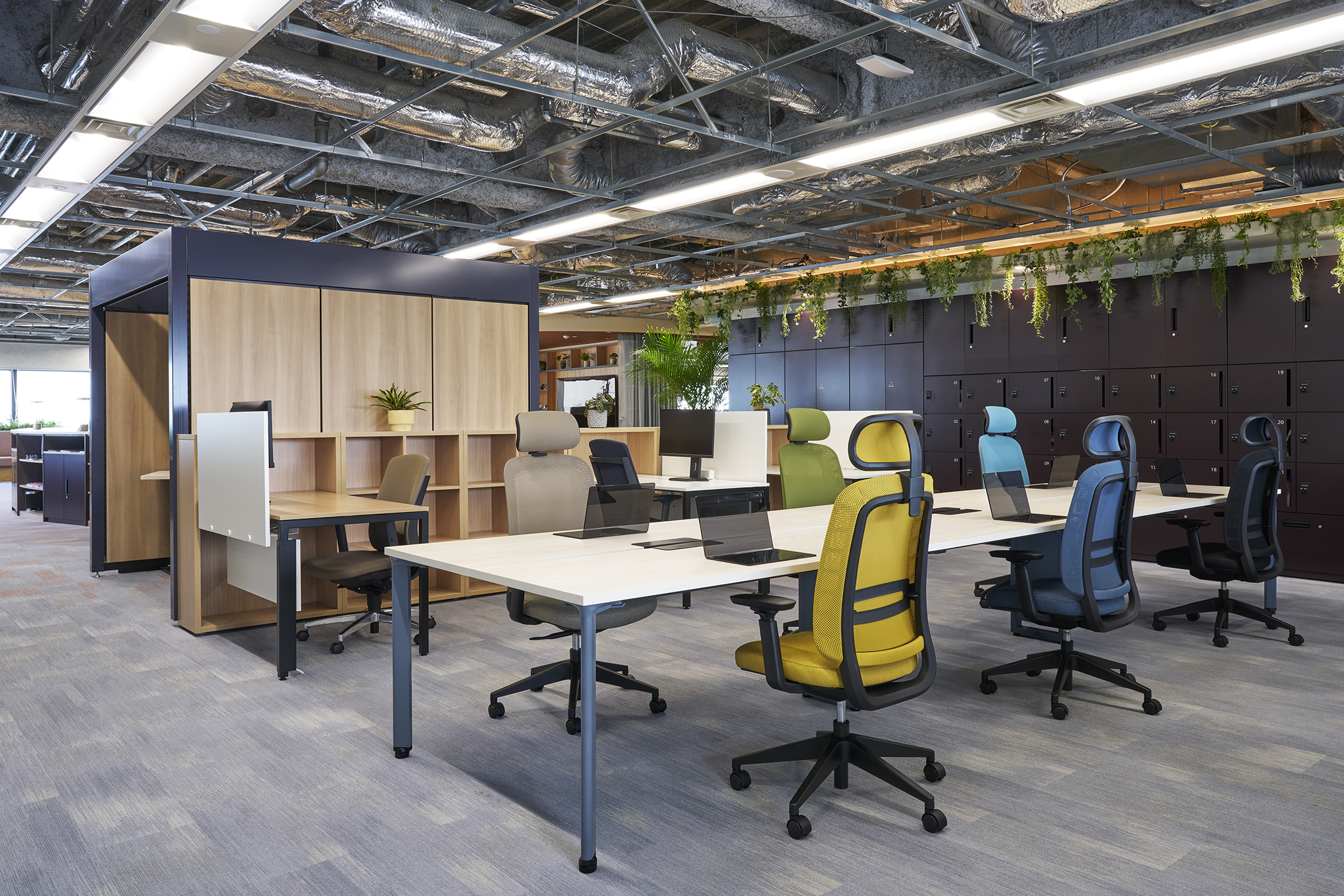 Modern open office with colorful ergonomic chairs, desks with laptops, and locker storage along the wall.