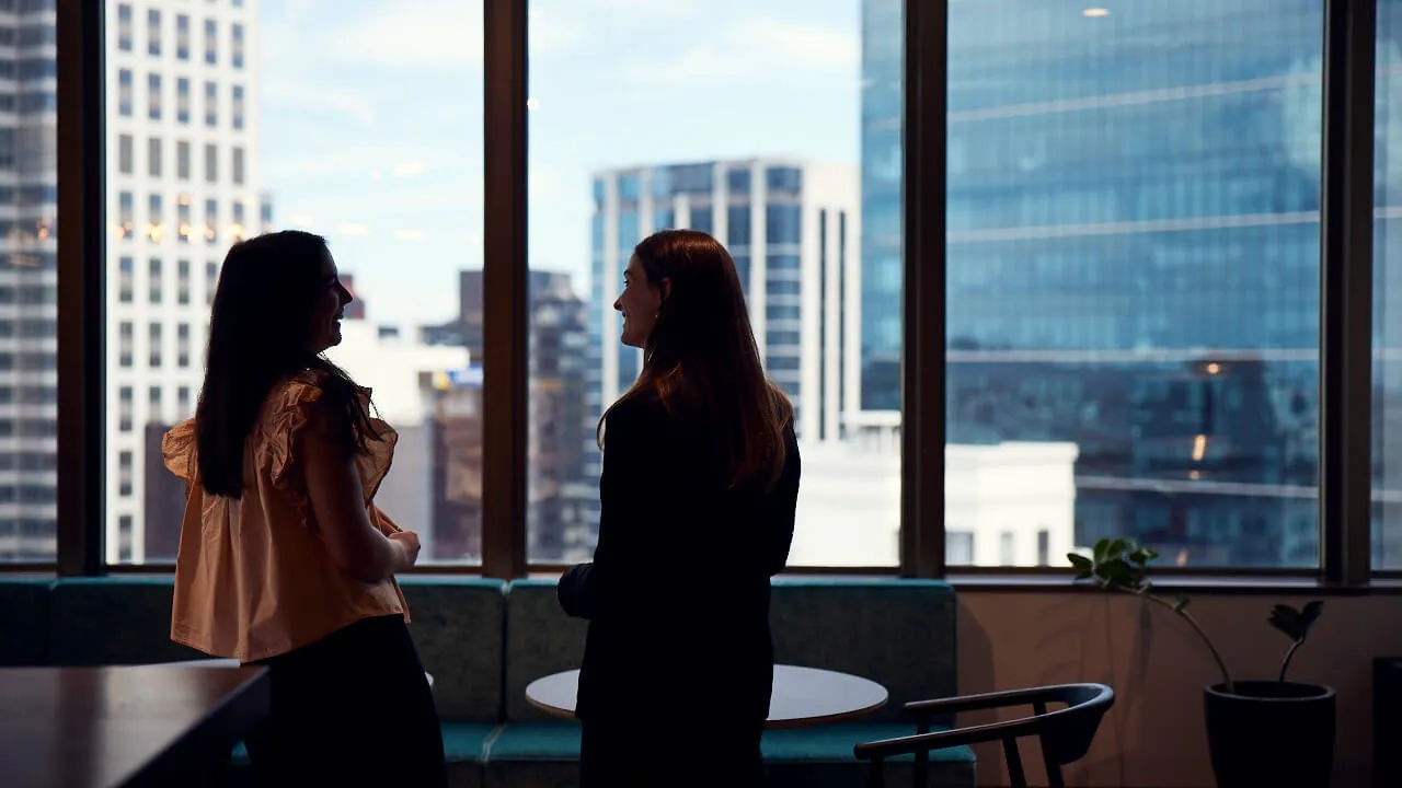 Two people talking next to a window