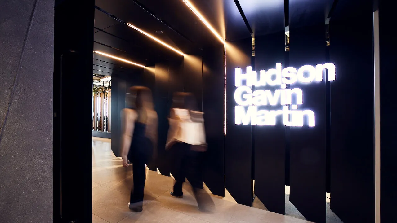 Two employees walking by an illuminated HGM sign