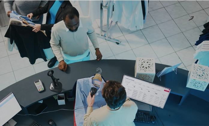 Vista aérea de um caixa de loja escaneando uma camisa azul para um cliente, com o monitor exibindo o sistema de vendas.