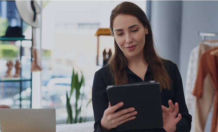 Mulher sorridente usando um tablet dentro de uma loja de roupas bem iluminada.