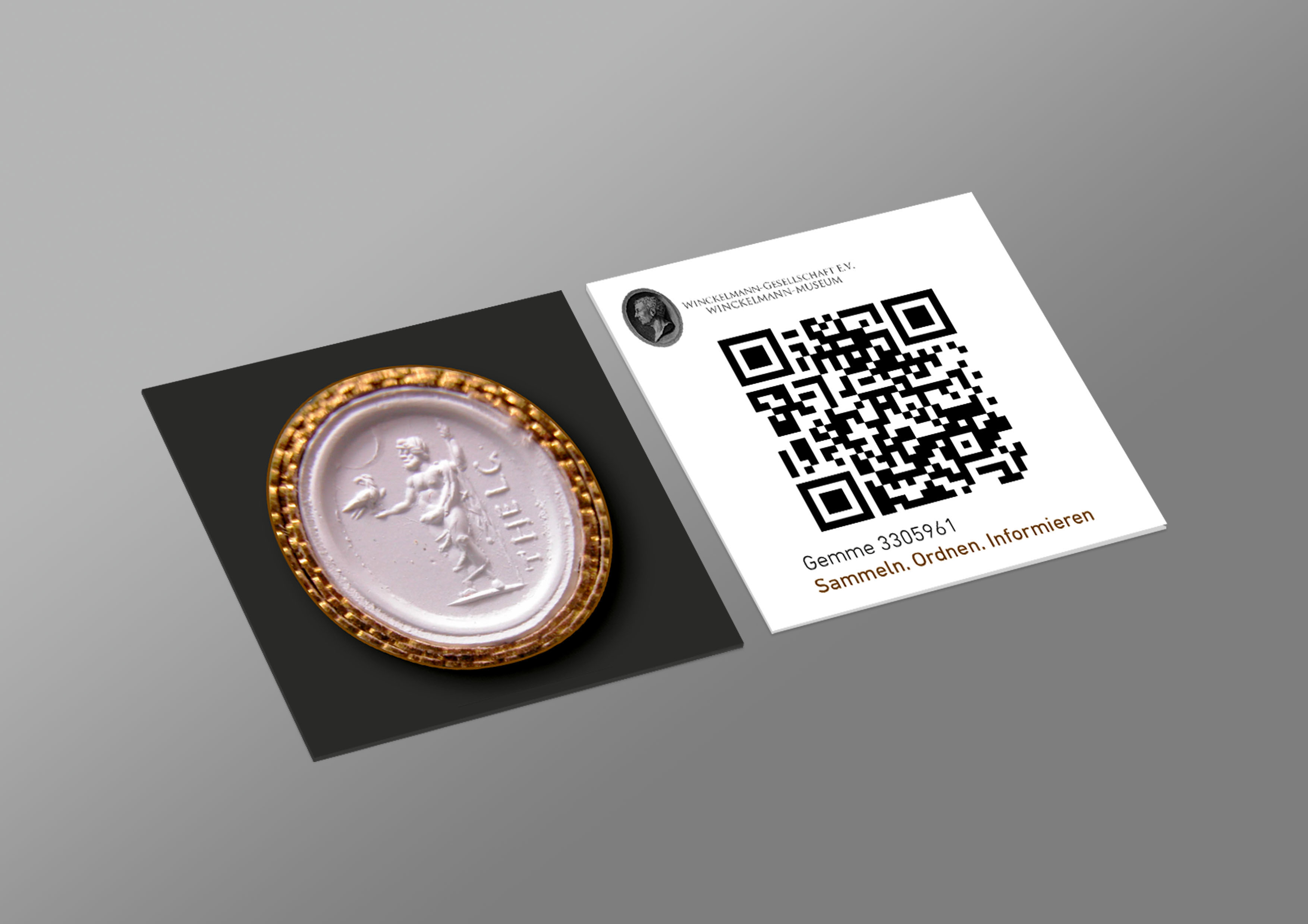 Oval gem with a relief of a standing figure holding a bird, next to a QR code card.
