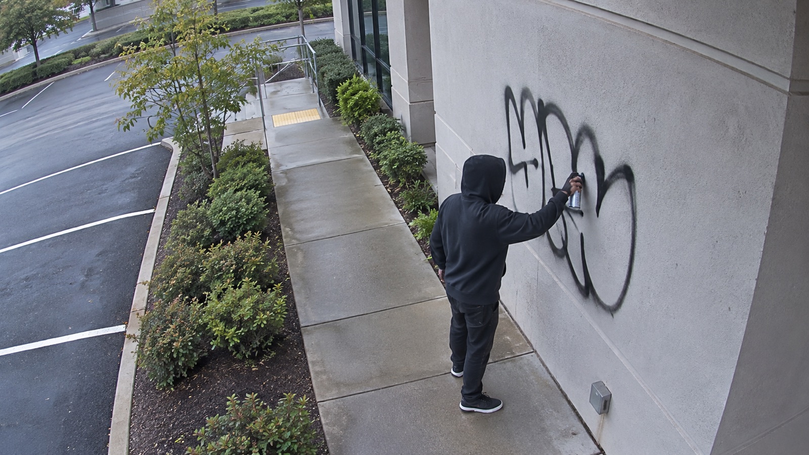 Security camera view of a person applying graffiti to a wall