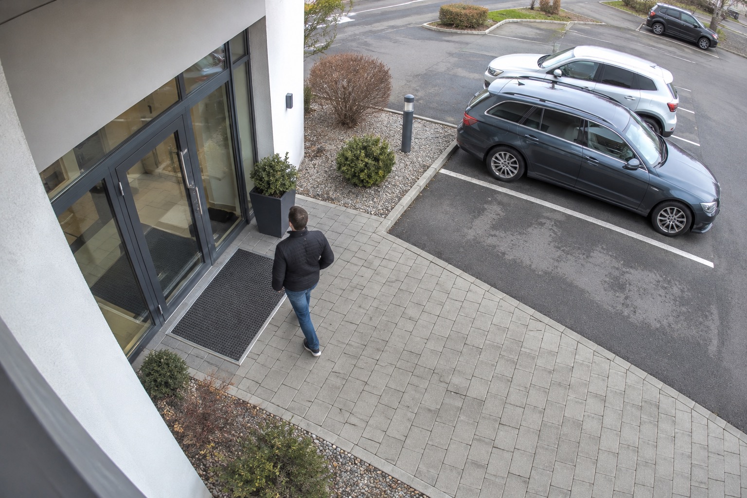 Illustrative high-mounted CCTV view of a building entrance and parking area