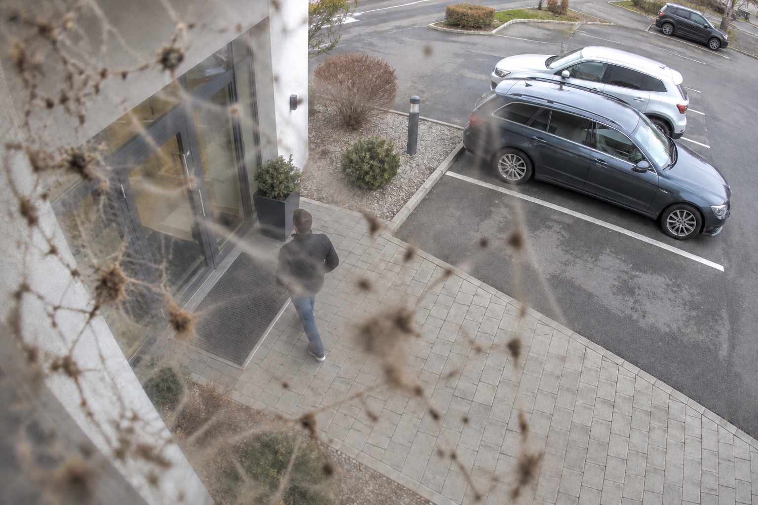 Illustrative high-mounted CCTV view of a building entrance and parking area