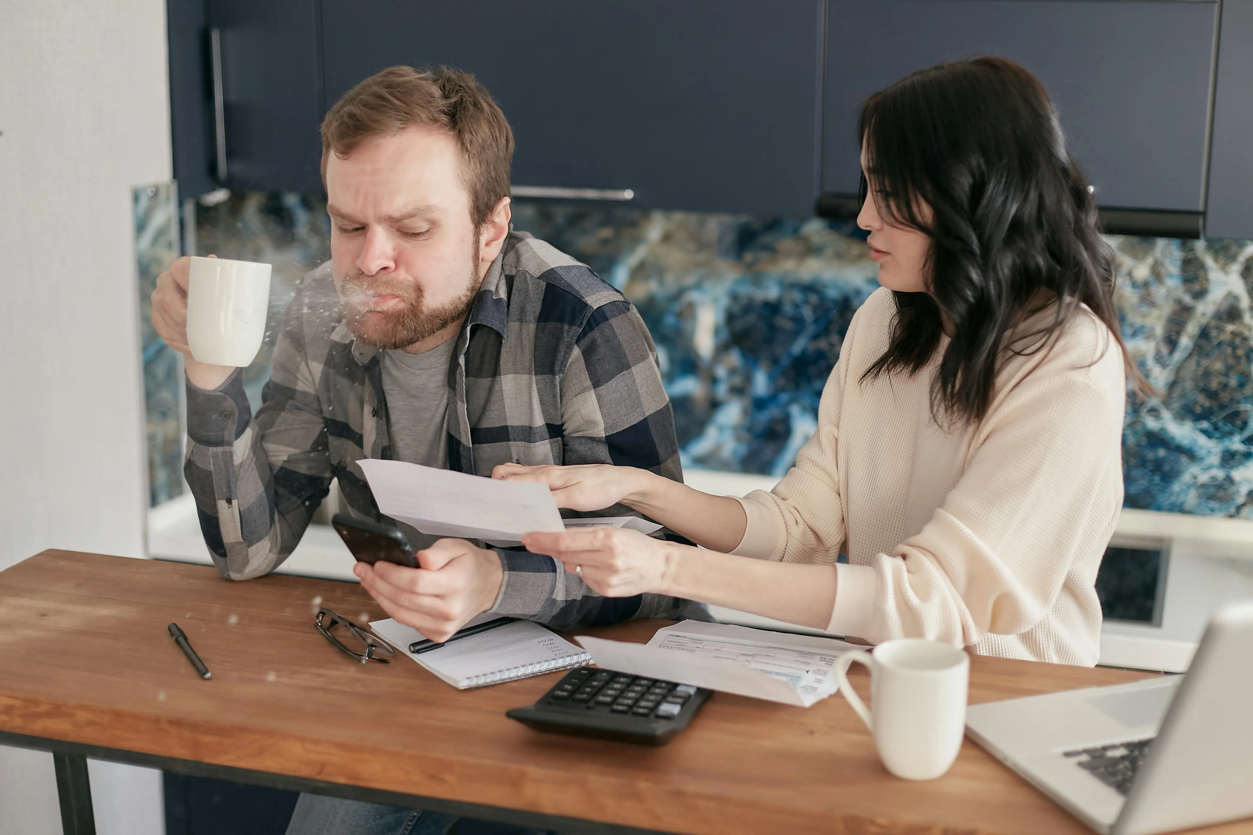 Man spitting out coffee looking at a form a woman is showing him