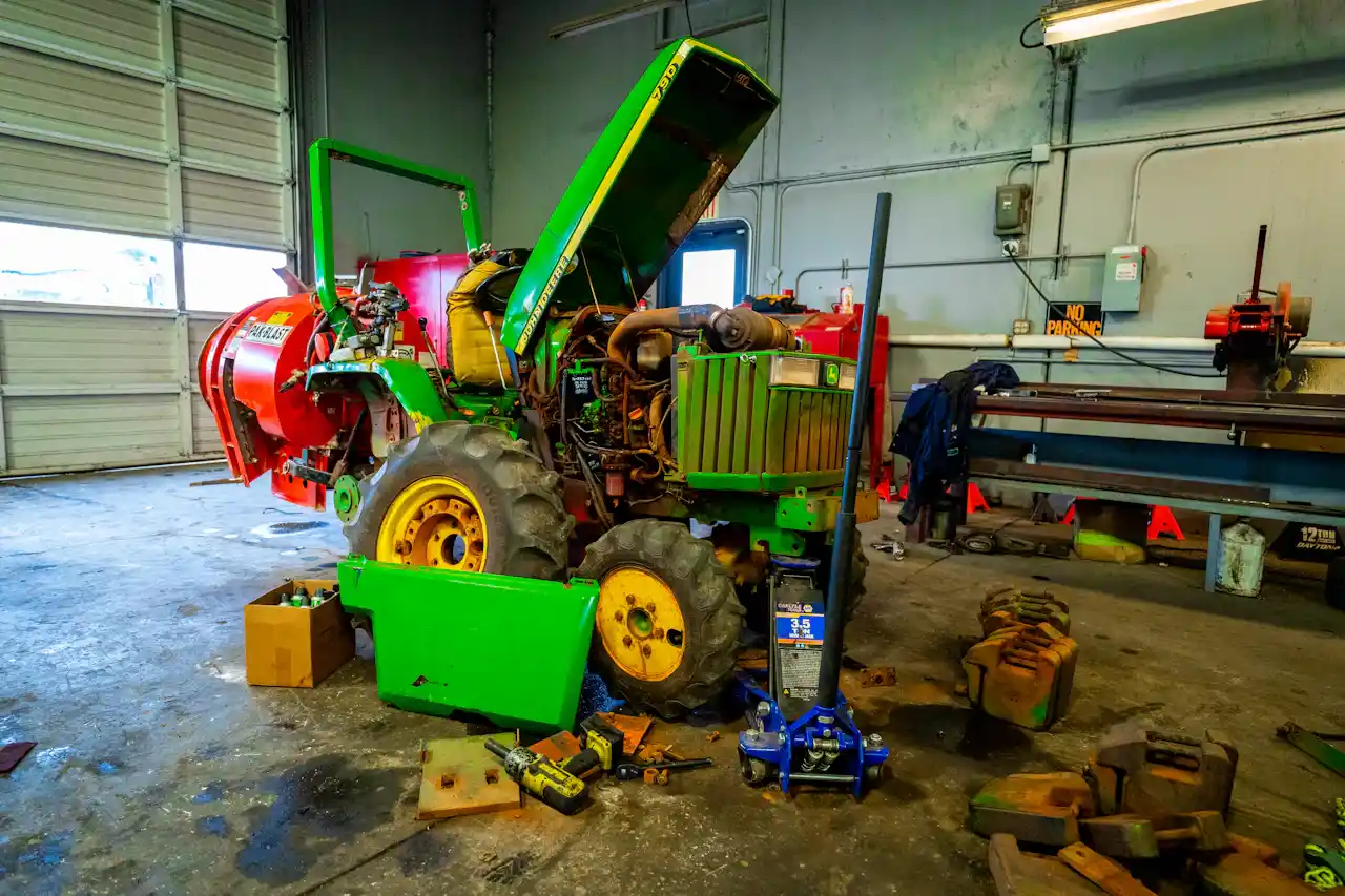 Tractor repair with the hood open, exposing the engine as tools and a floor jack surround the heavy-duty equipment.