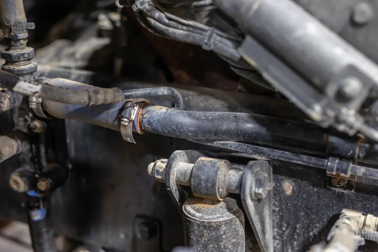 Close-up of a heavy-duty truck hydraulic hose connected with metal clamps and fittings, showing signs of wear and corrosion that may indicate the need for hydraulic hose inspection, repair, or replacement.
