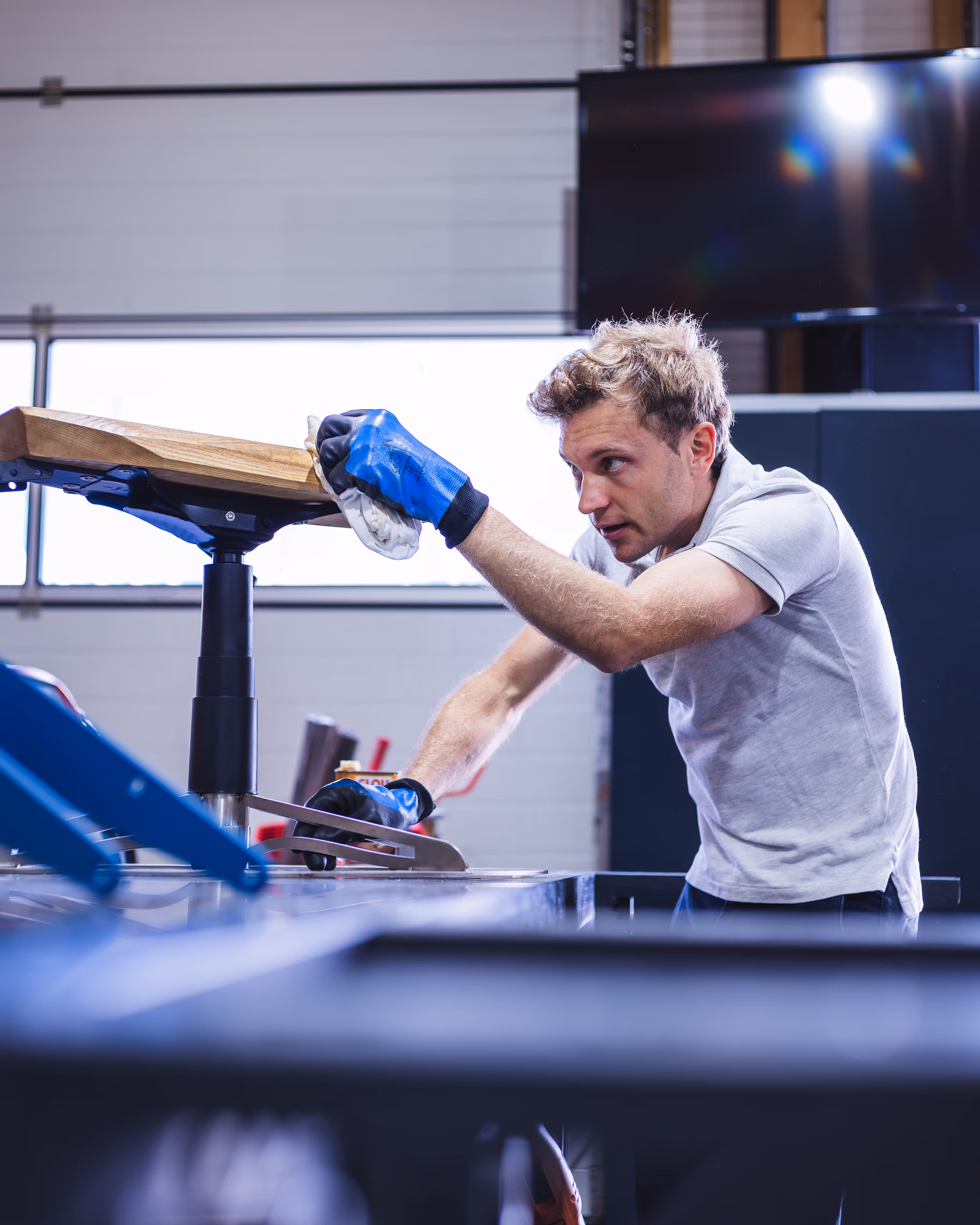 Mann mit blauen Arbeitshandschuhen poliert einen Sandkastenbagger in einer Werkstatt.