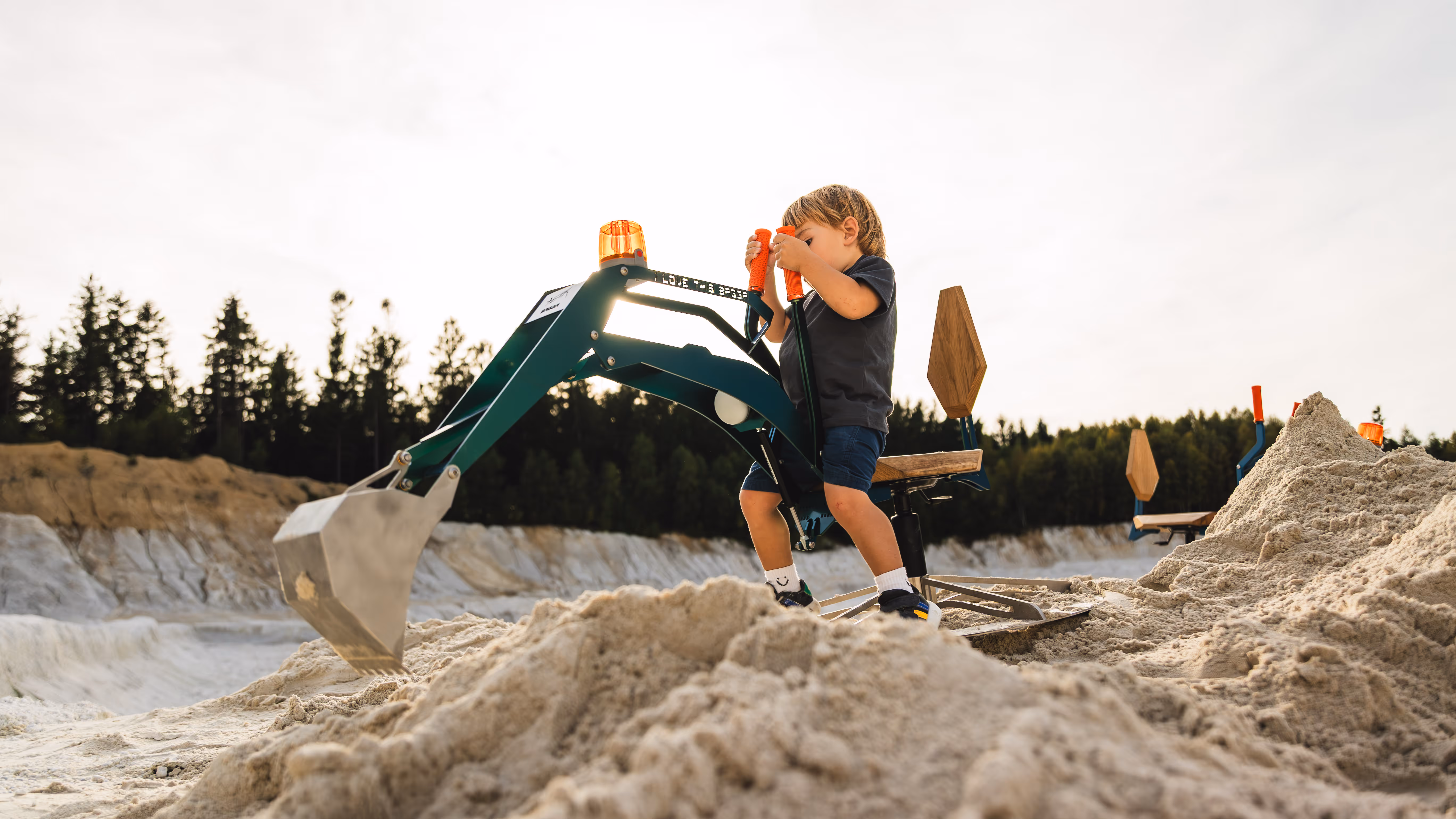 Kleiner Junge sitzt auf einem grünen Kinderspielzeug-Bagger im Sand und spielt.