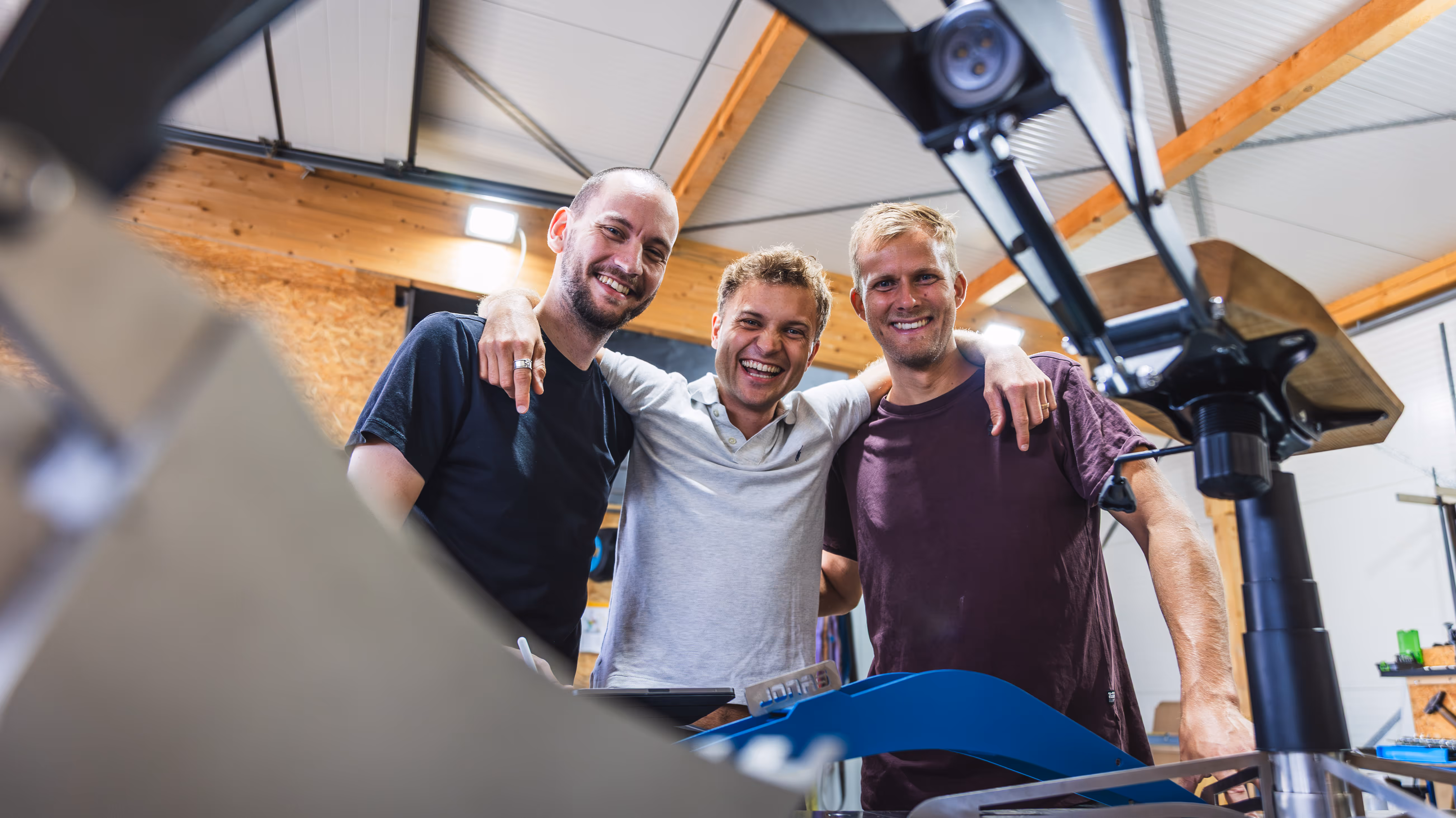 Die Mitglieder der HEFA CREW stehen in einer Werkstatt mit Holz- und Metallgeräten und lächeln in die Kamera.