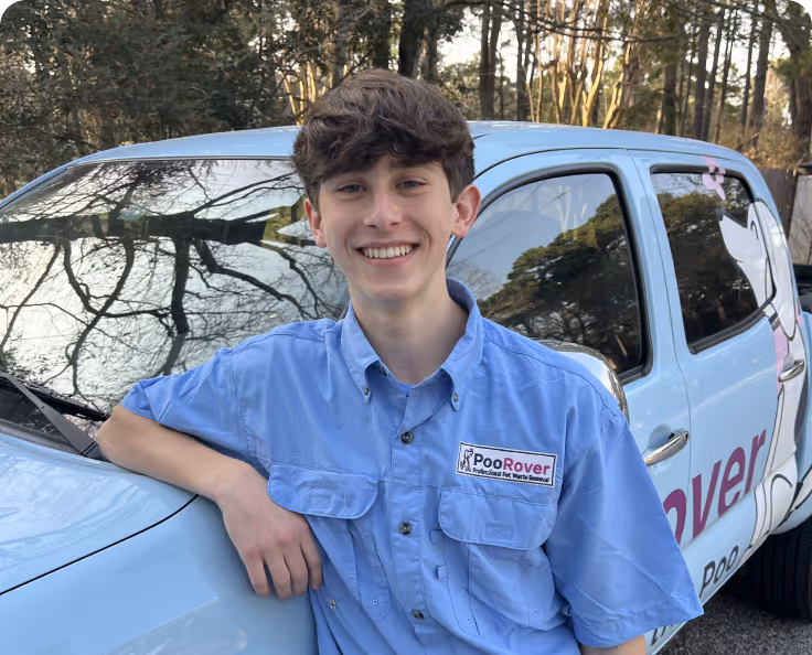 Smiling young man in blue PooRover uniform leaning on a light blue PooRover truck with a cartoon dog graphic on the door.