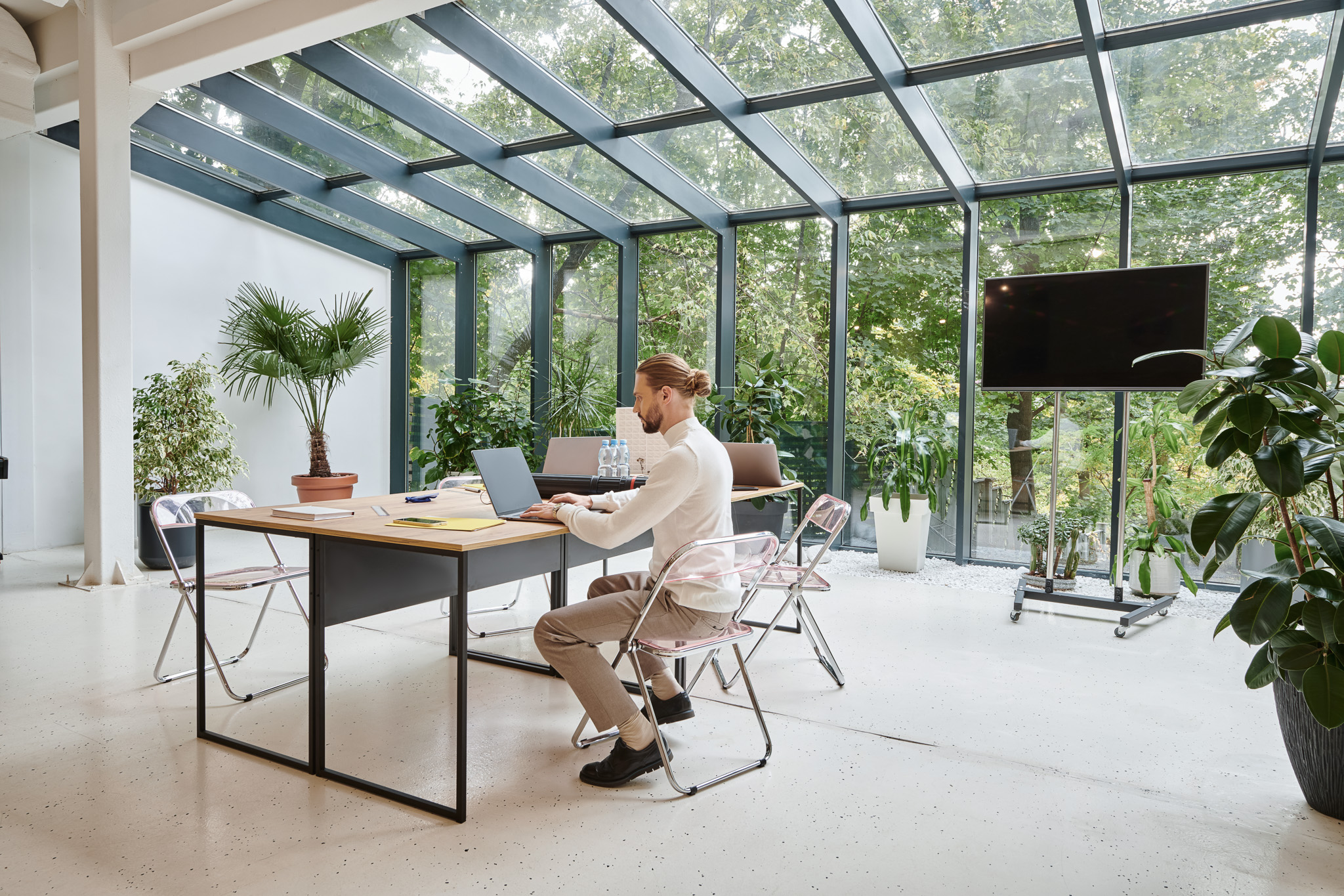 Modernes Büro mit großen Glasfronten, Pflanzen und energieeffizienter Medientechnik: Green AV-Lösung mit nachhaltigem Display und umweltfreundlicher Ausstattung.