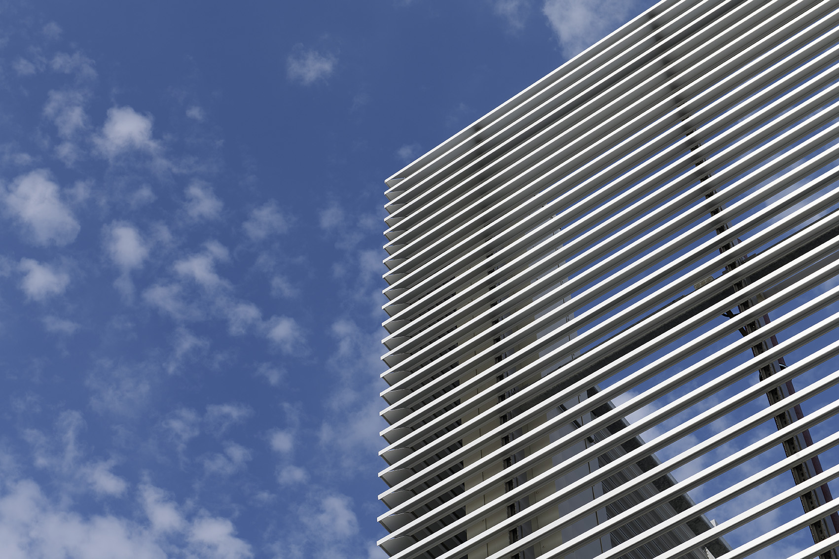 Moderne bygning med vandrette metalriste foran en klar blå himmel med få skyer.