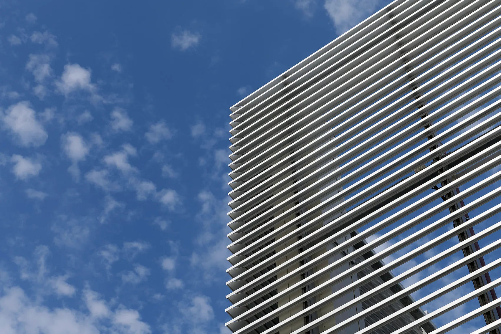 Moderne bygning med vandrette metalriste foran en klar blå himmel med få skyer.