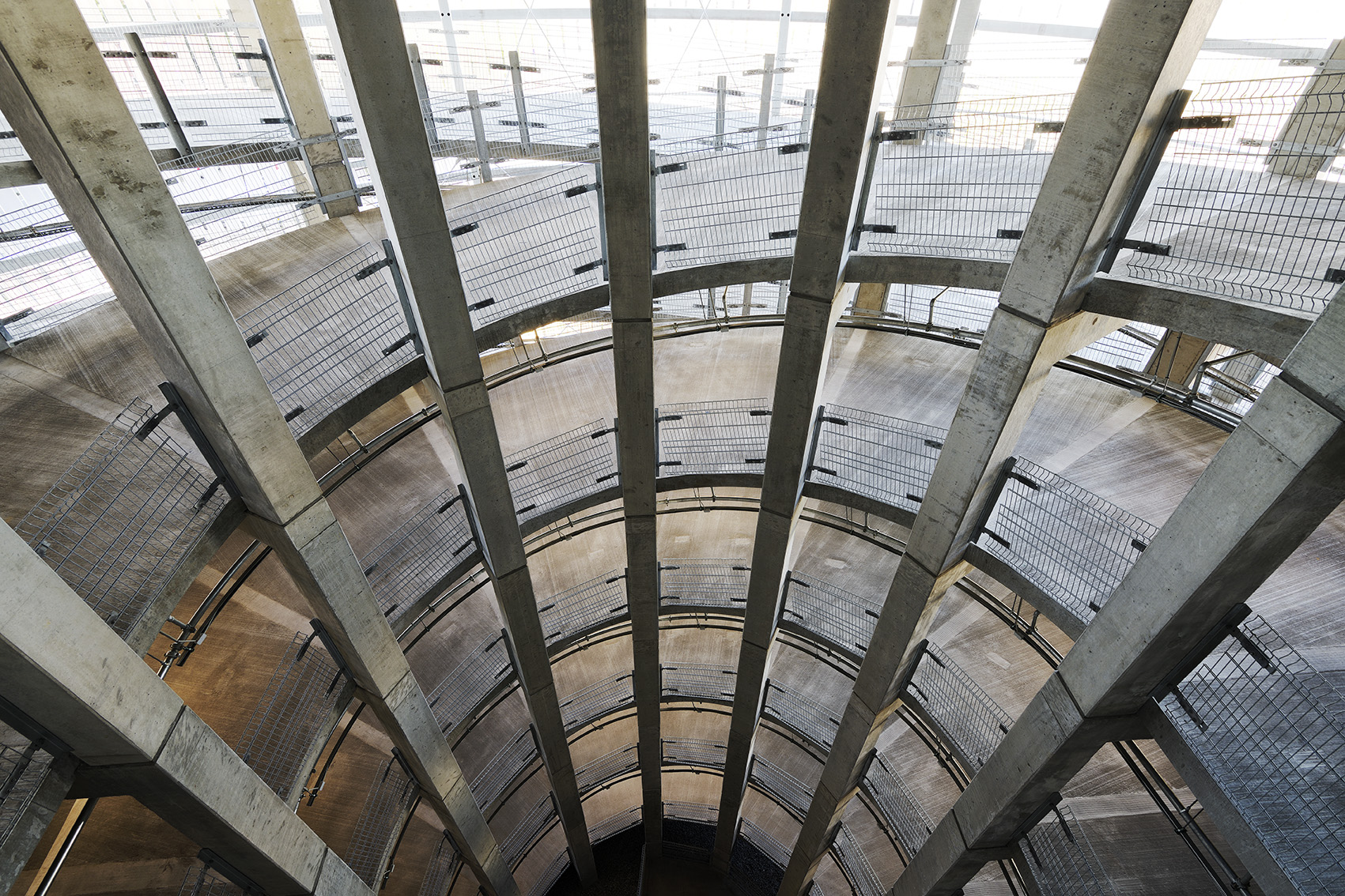 Indvendigt kig ned i en cirkulær betonrampestruktur med metalgelændere.