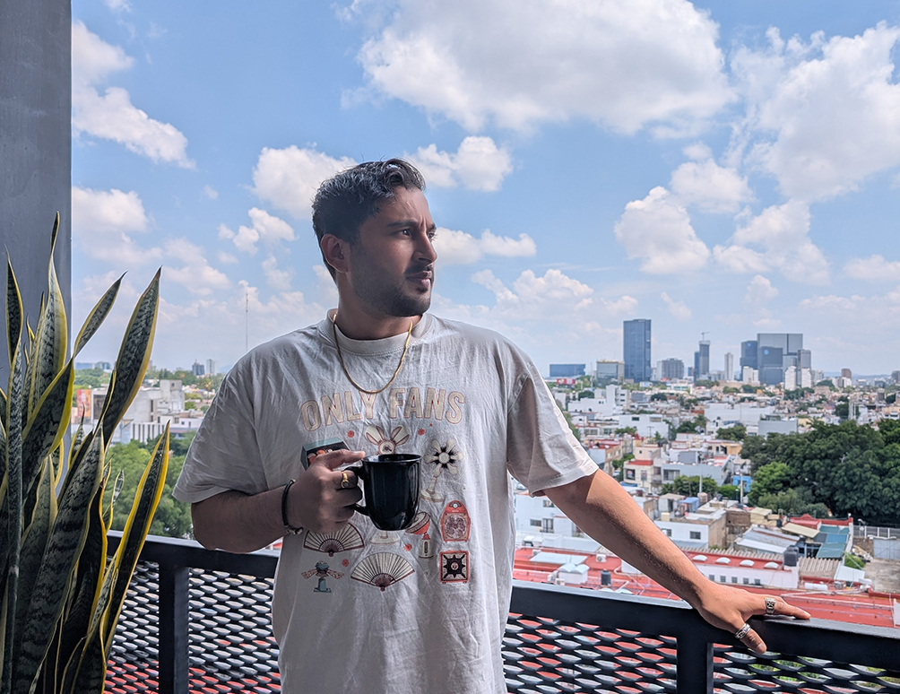 Nikhil Sharma on a rooftop terrace with a coffee, overlooking a city skyline during a remote work trip