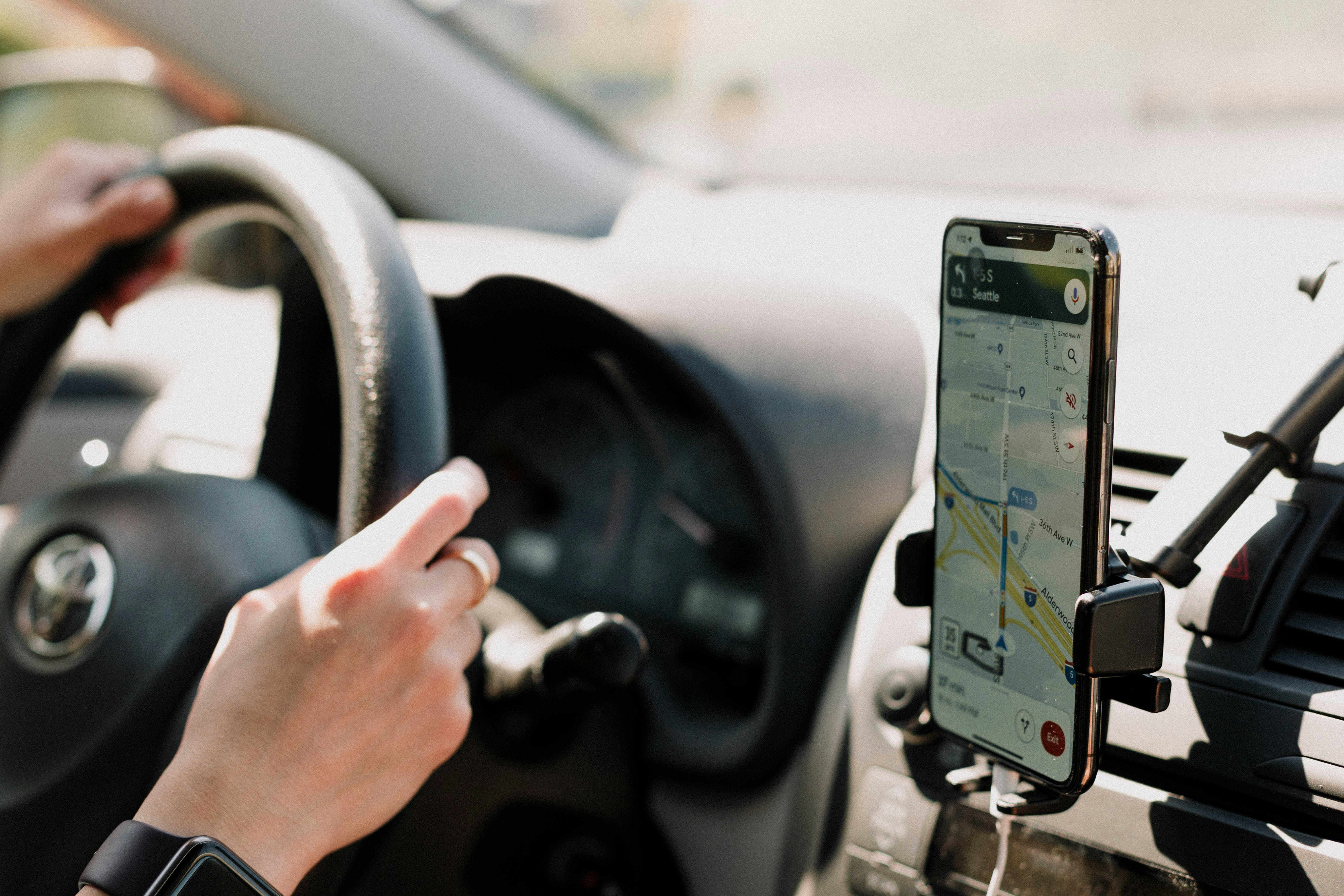 Person driving a car with Google Maps navigation open on a mounted smartphone screen, Moncton, nb.