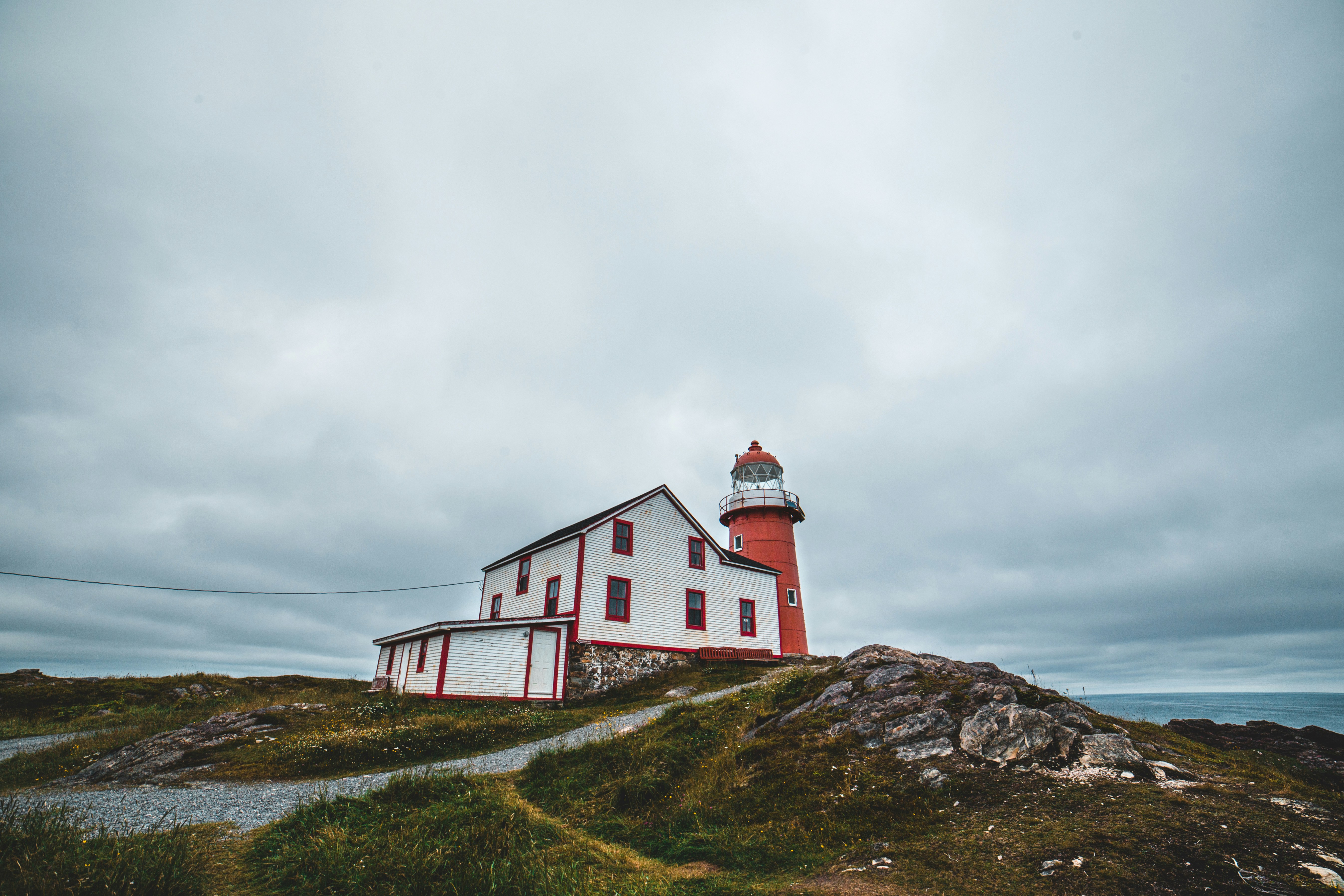 Historic red and white lighthouse on a grassy hilltop under an overcast sky in Atlantic Canada.