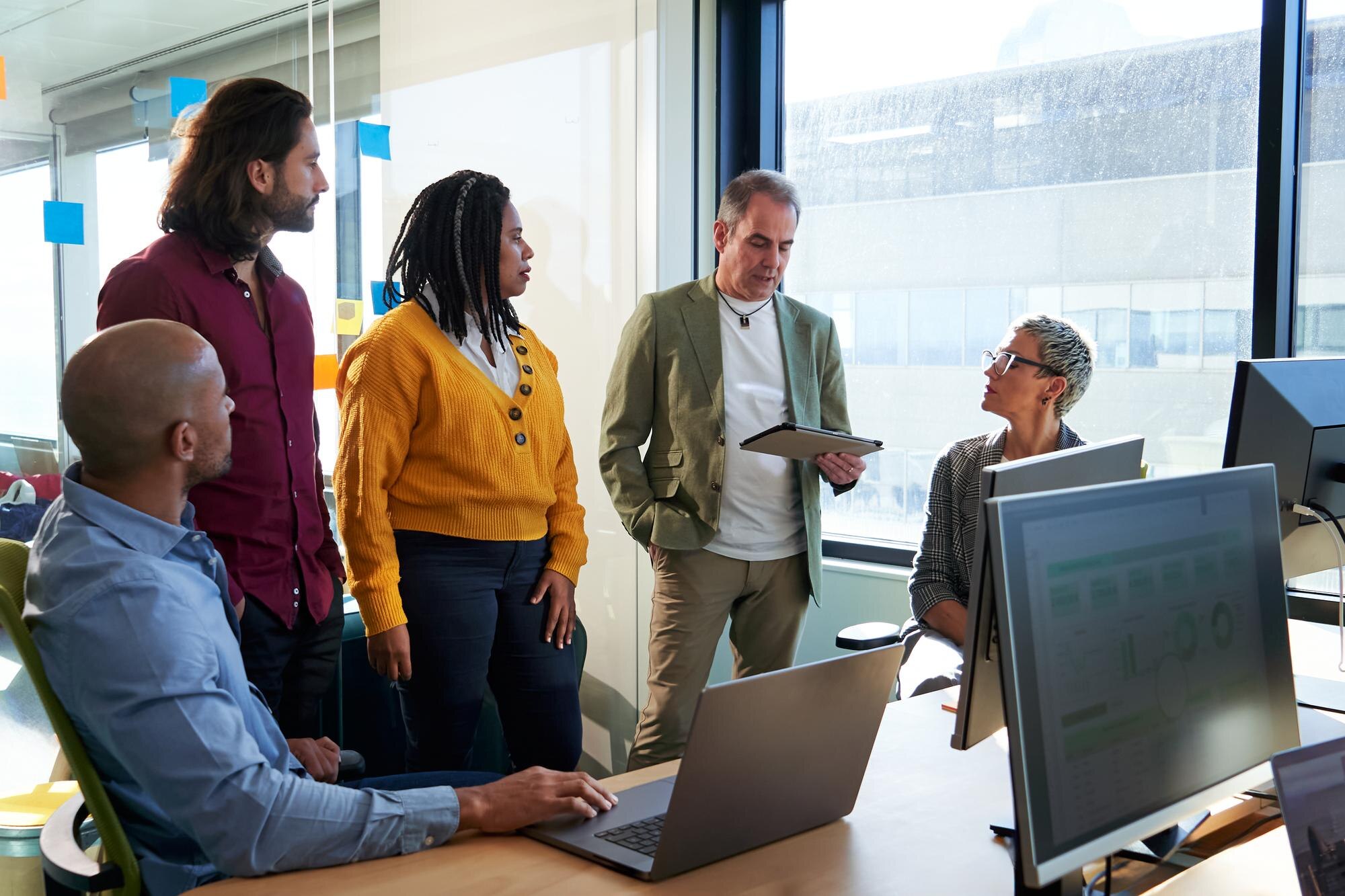 Diverse team having a discussion around a desk with laptops in NB, canada.