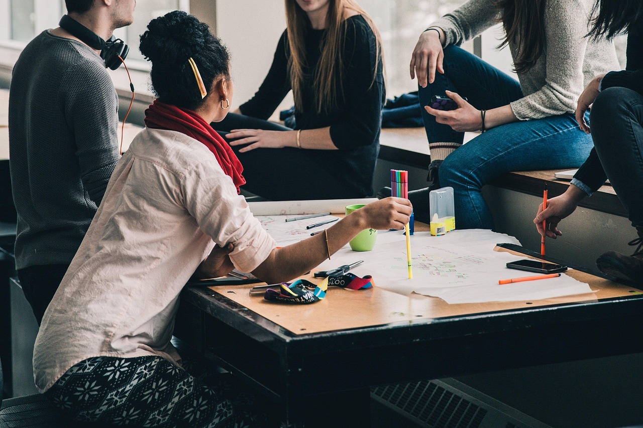 Group of young adults collaborating at a table with papers, pens, and coffee cups during a casual team meeting.