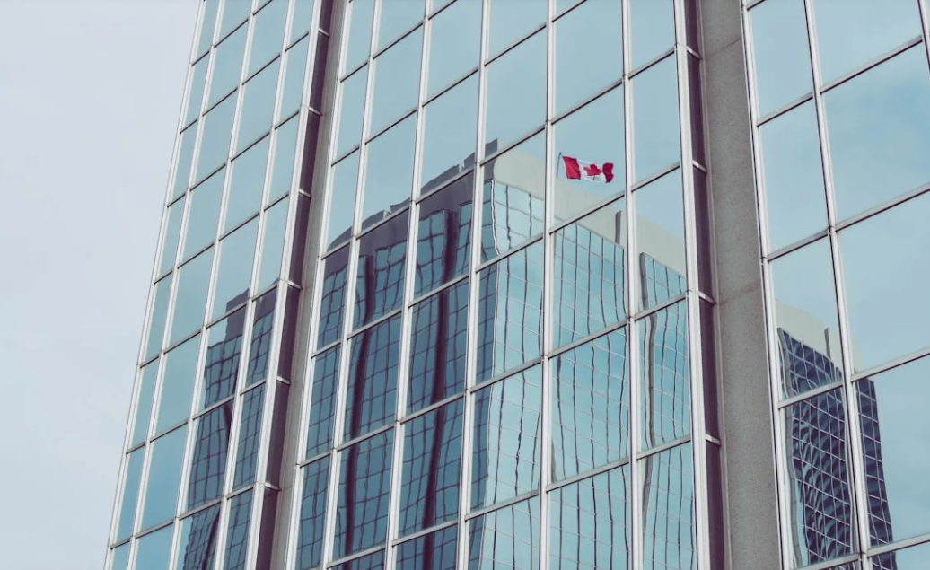 Reflection of Canadian flag and modern high-rise buildings on glass windows of an office tower.