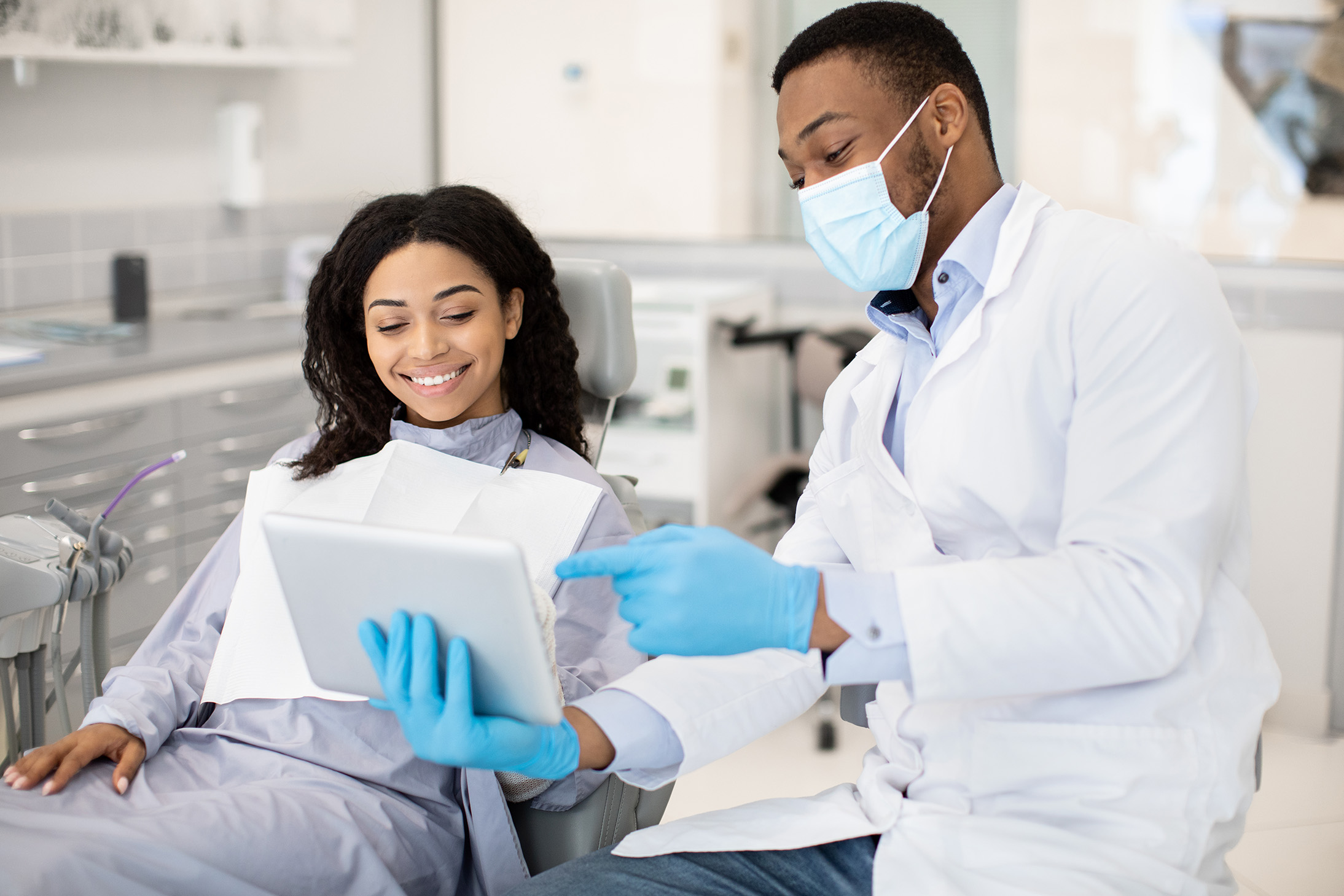 Dentist showing treatment information on a tablet to a patient seated in a dental chair.