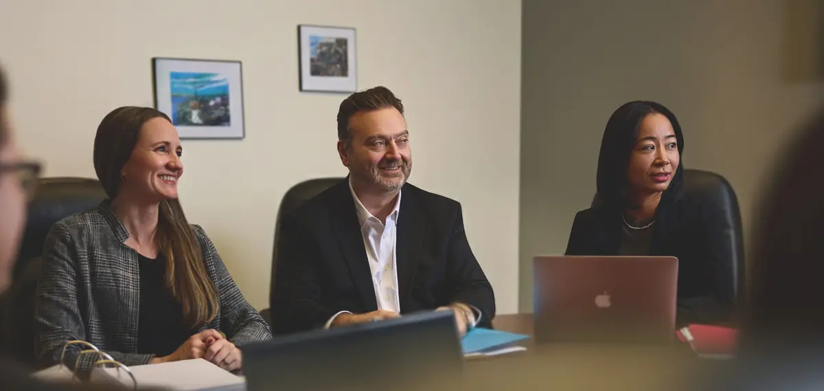 Three CLG Injury Law lawyers seated at a conference table during a professional firm meeting with laptops open