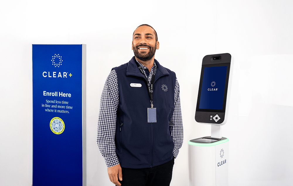 CLEAR Ambassador standing between EnVe Pod and CLEAR Plus sign at airport