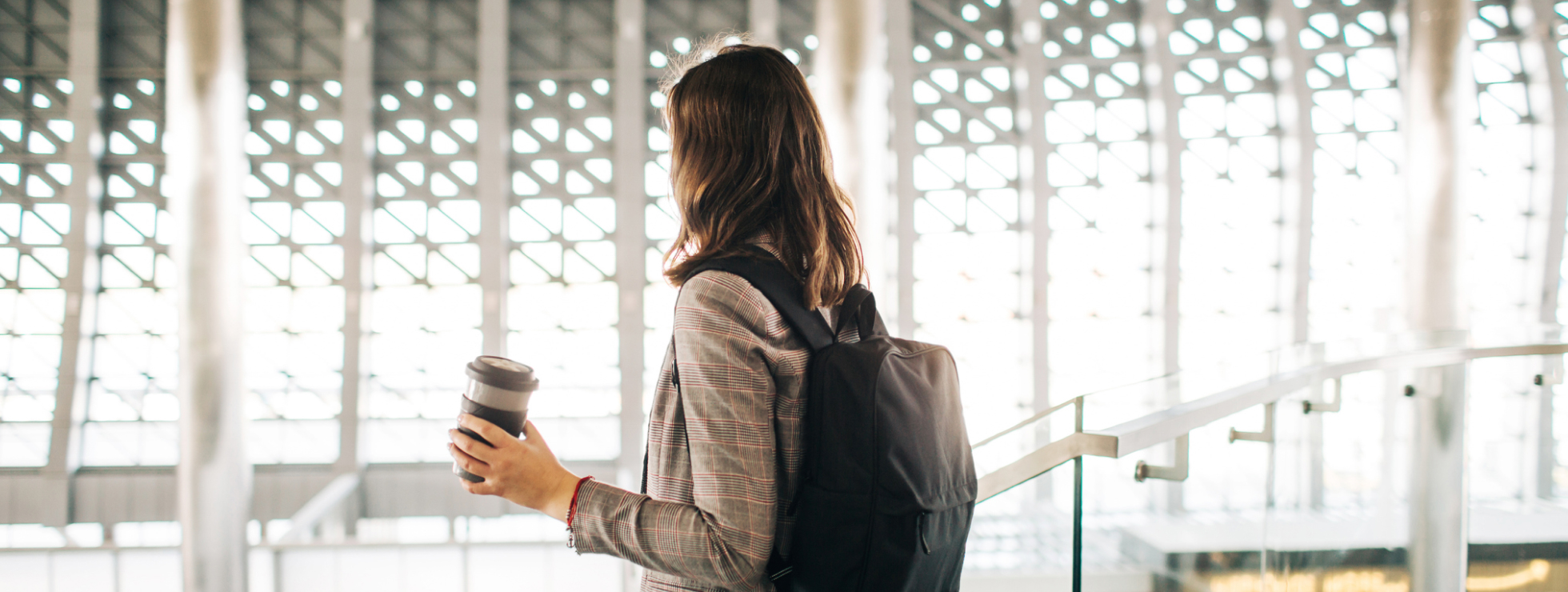 Photo of the back of a traveler with a backpack holding a coffee cup in the airport 