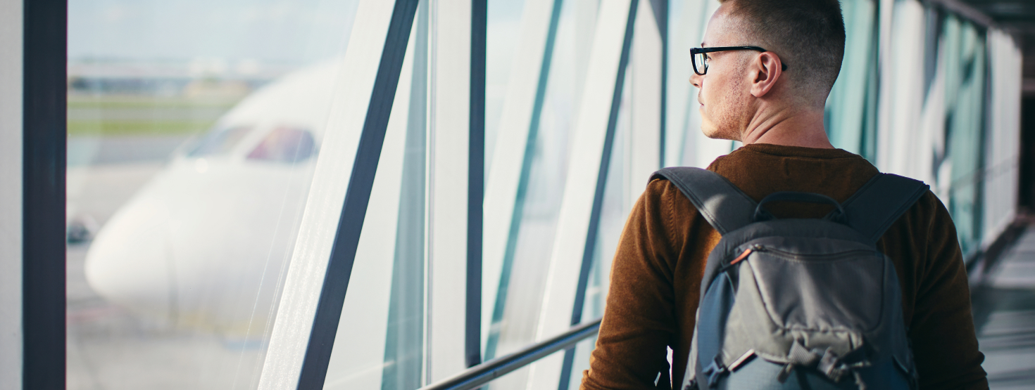Man with a backpack looking at an airplane and walking on the passenger boarding bridge