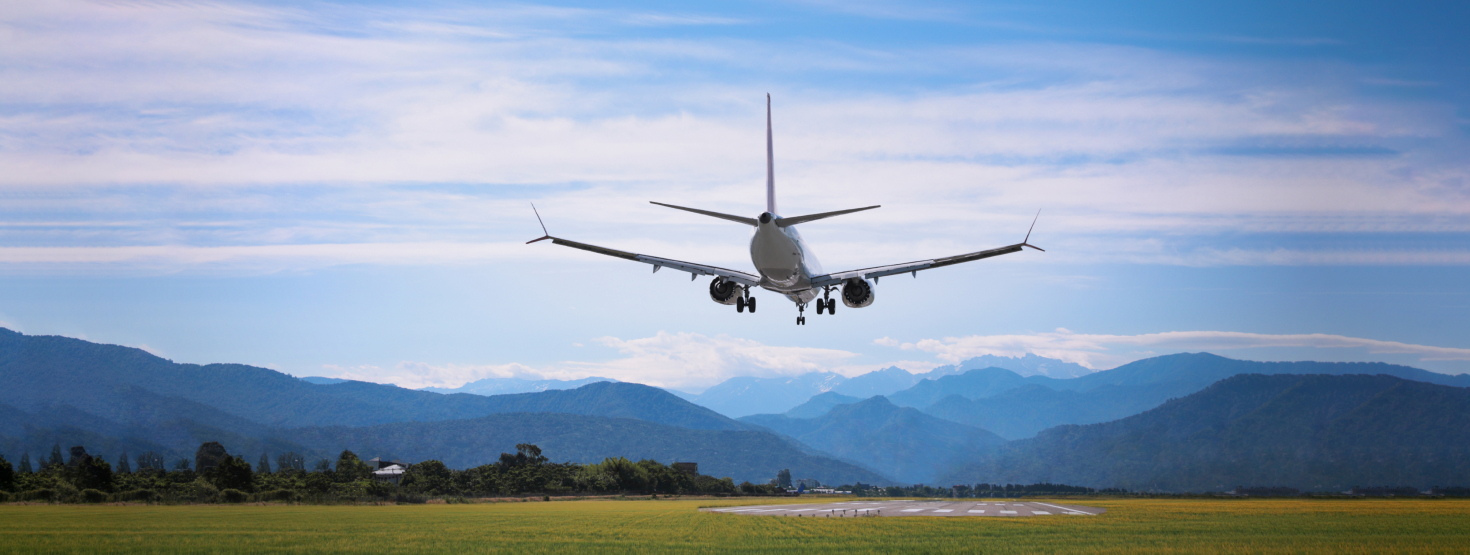An airplane landing onto runway with mountains in the backdrop