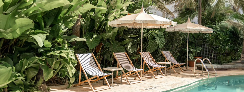 Beach chairs and umbrella in front of greenery and next to relaxing pool