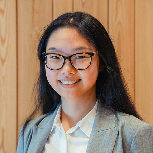 A woman wearing glasses standing in front of a wooden wall.