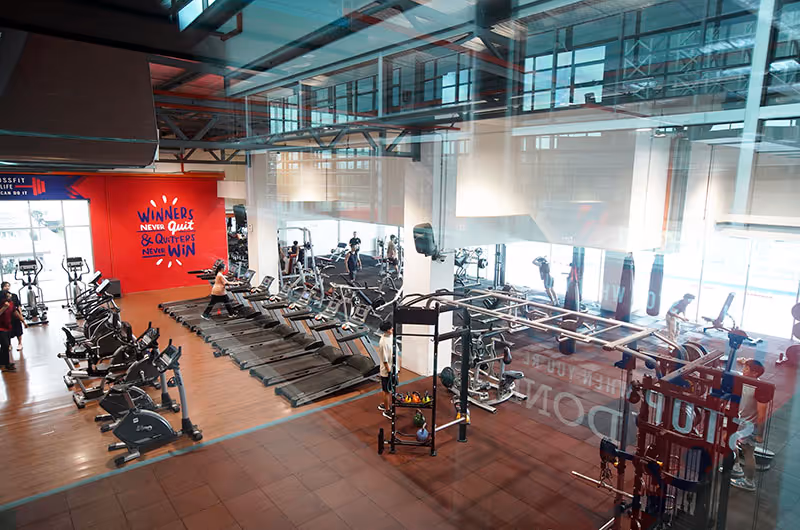 Interior view of a gym with treadmills, stationary bikes, weight machines, and people exercising.