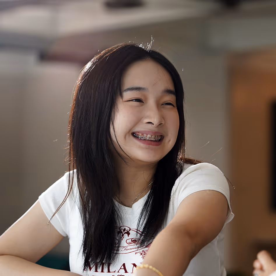Young woman with long dark hair smiling and showing braces, wearing a white t-shirt.