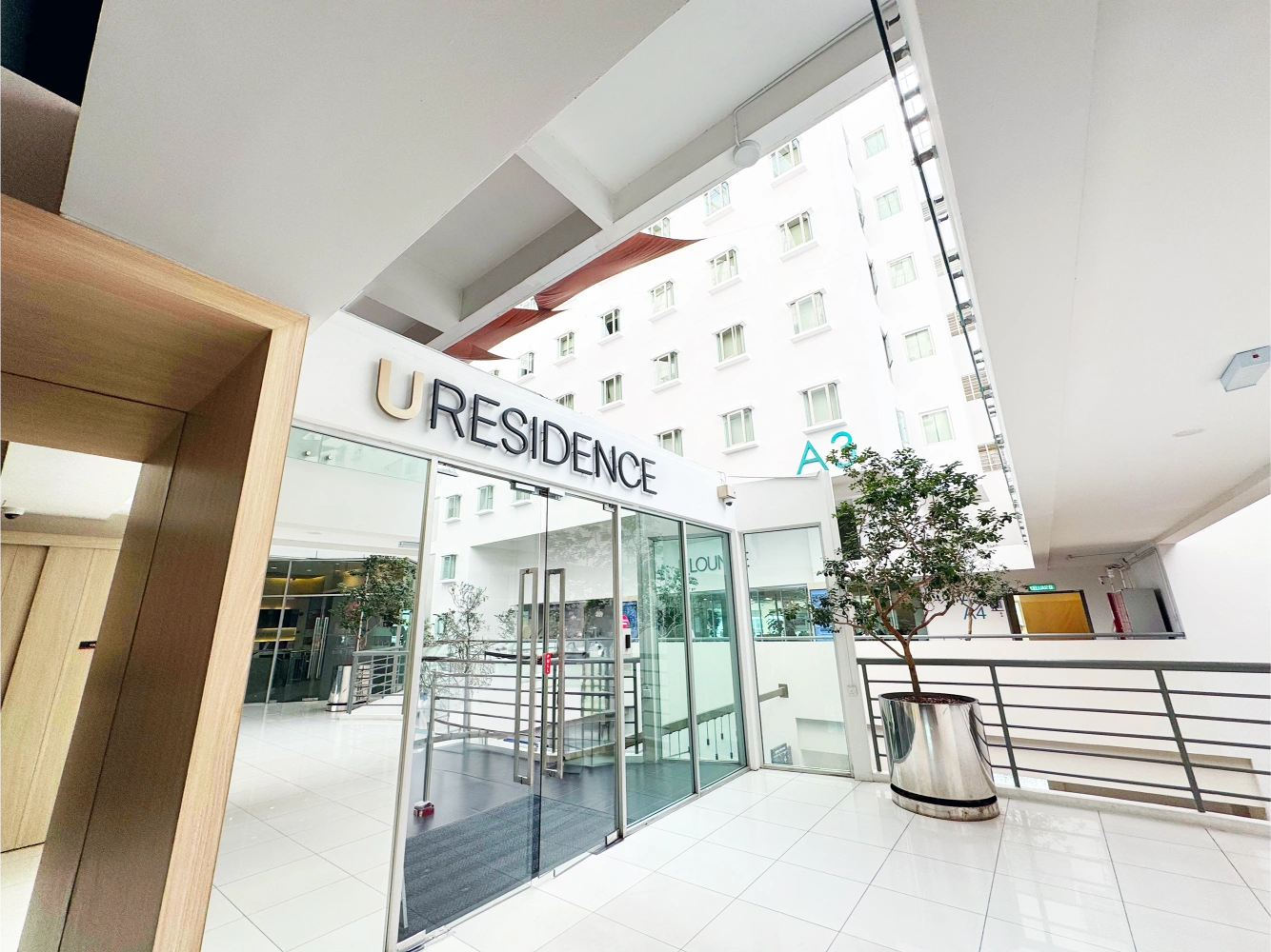 Entrance to U Residence with glass sliding doors, white tiled floor, and a potted plant inside a modern building.