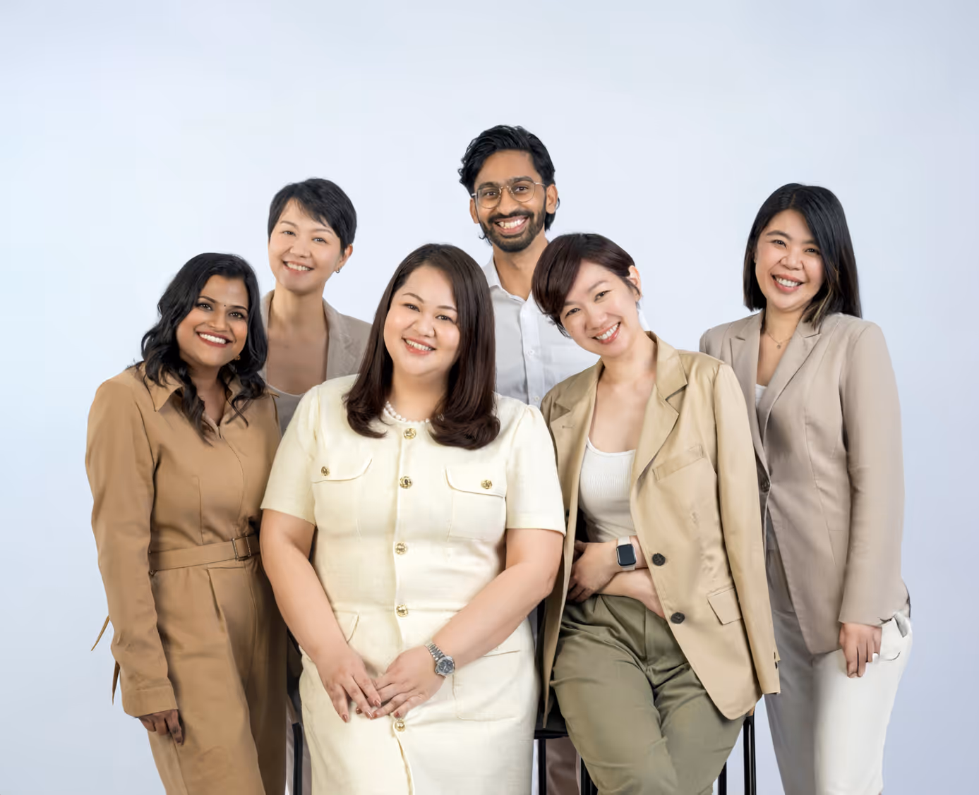 Smiling diverse group of six professionally dressed people posing against a plain background.