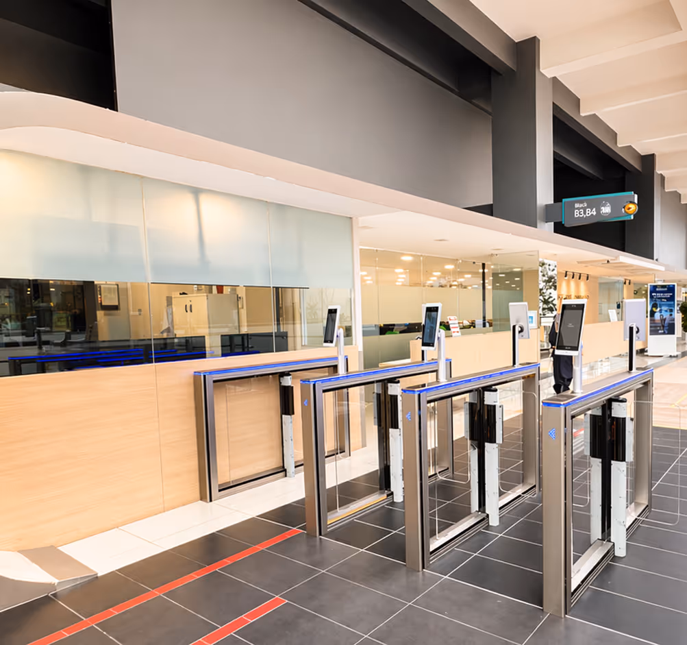 Modern security entrance with multiple stainless steel turnstiles and digital access screens in a bright office lobby.