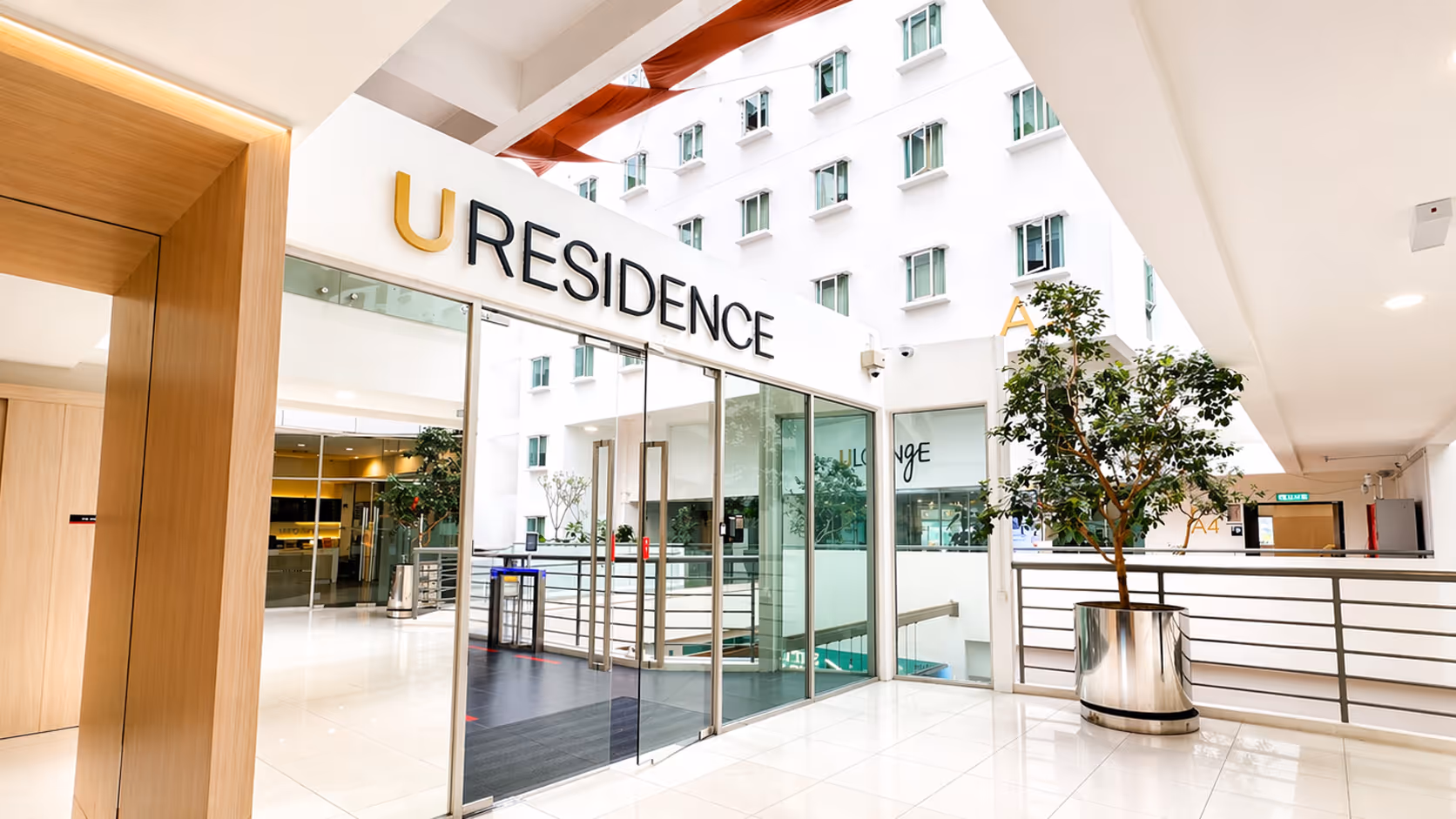 Bright modern interior entrance with glass doors labeled 'URESIDENCE' and a large potted plant on the right.