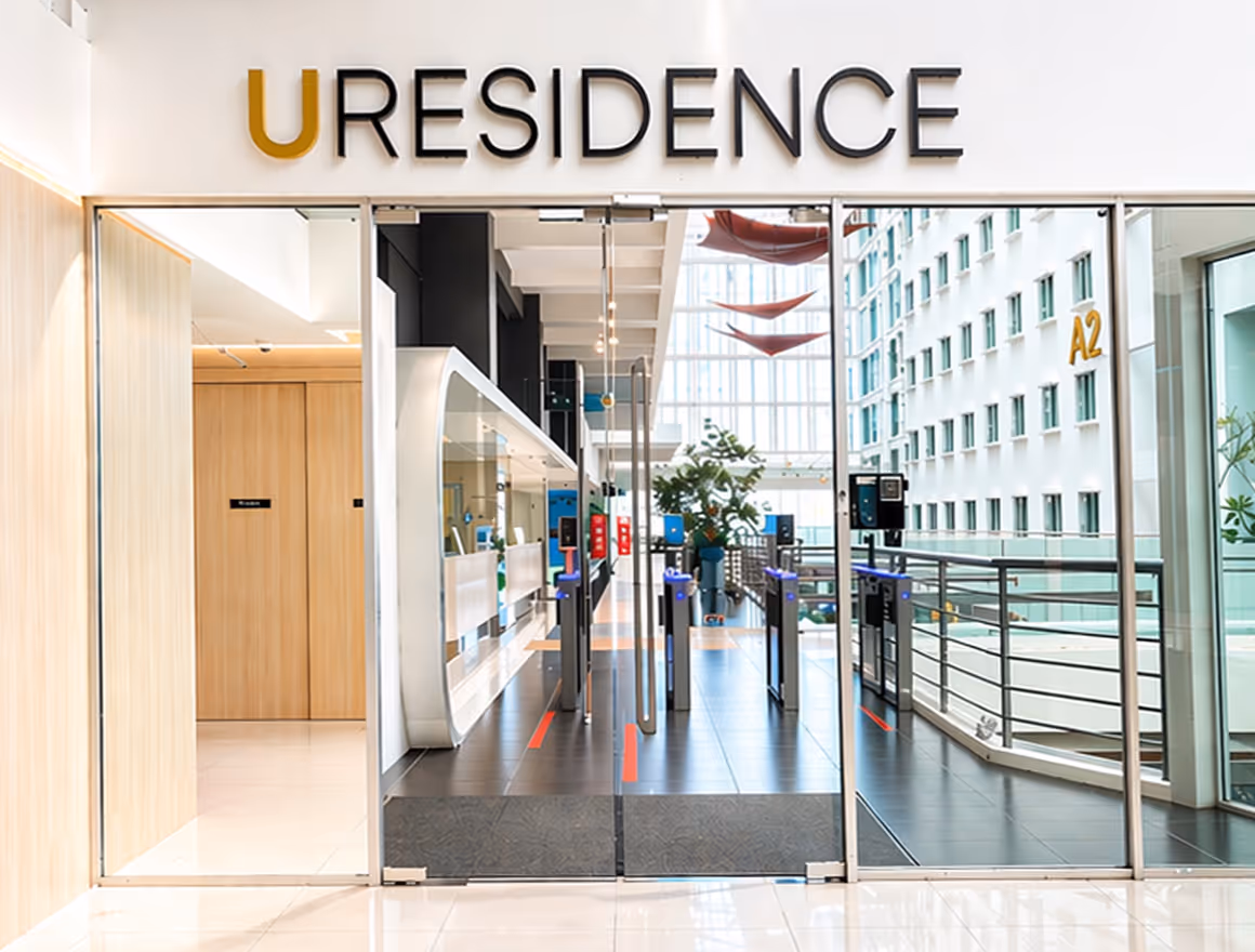 Modern entrance to U Residence with glass doors, turnstile access, and bright interior with plants and windows.