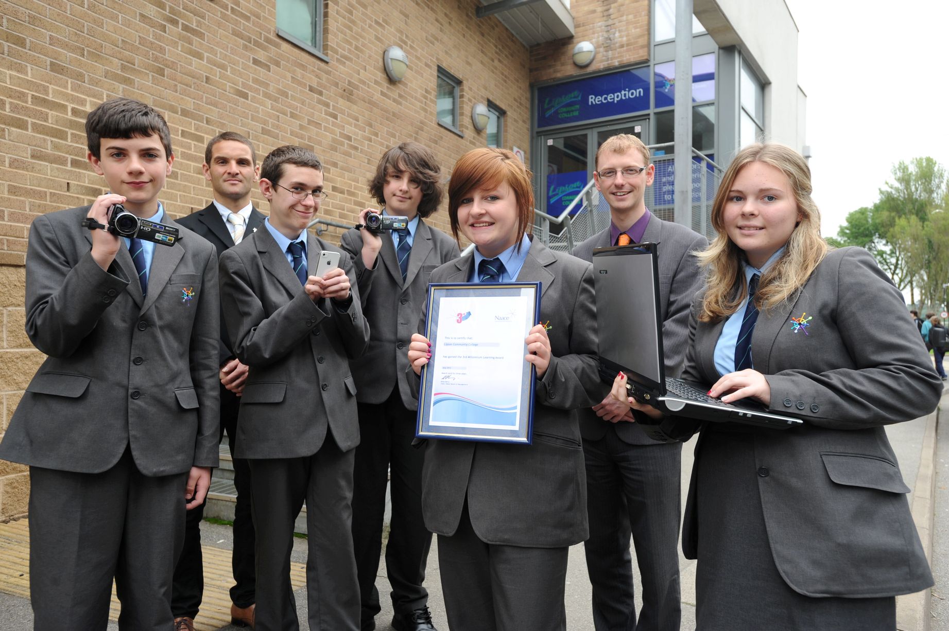 Students holding video cameras and an award. 