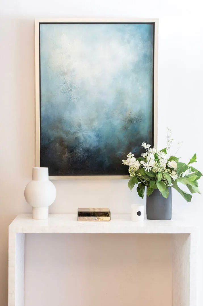 hallway table with flowers and vases beneath a blue painting