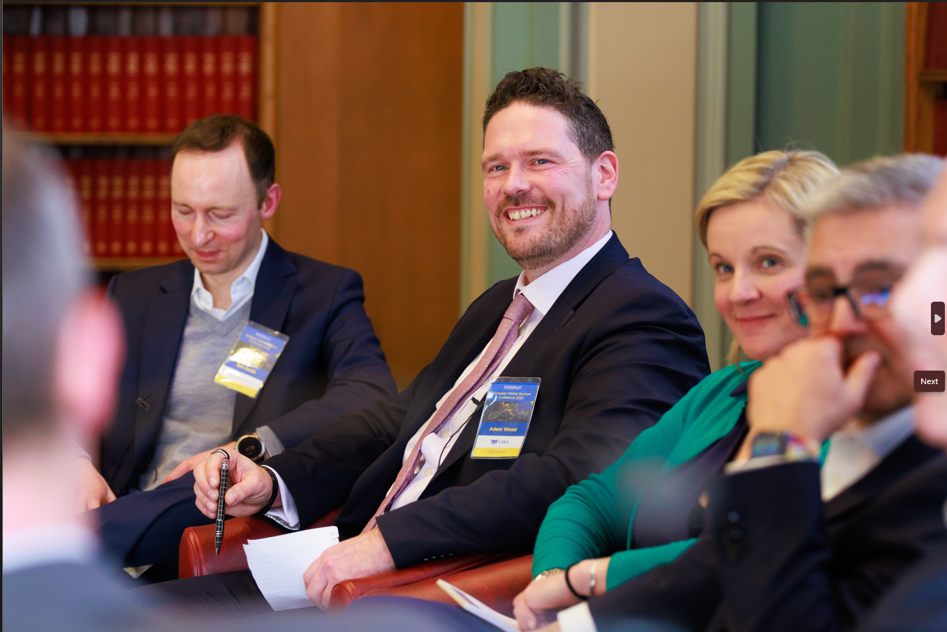 Adam Wood of Turquoise and LSEG smiles on a panel at the 2023 Rosenblatt Securities European Market Structure Conference, held in a classic library room.