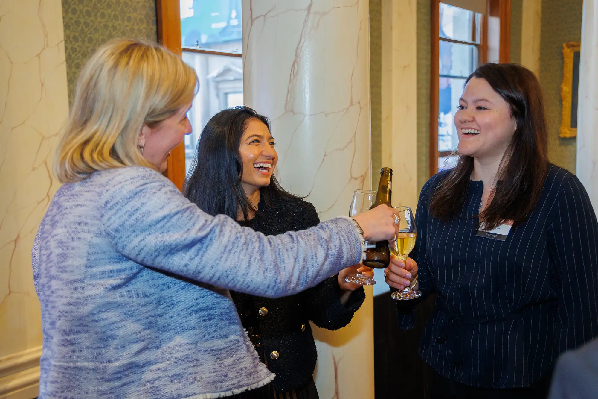 Three professional women network and toast with drinks during the 2025 Rosenblatt Securities European Market Structure Conference in a formal setting.