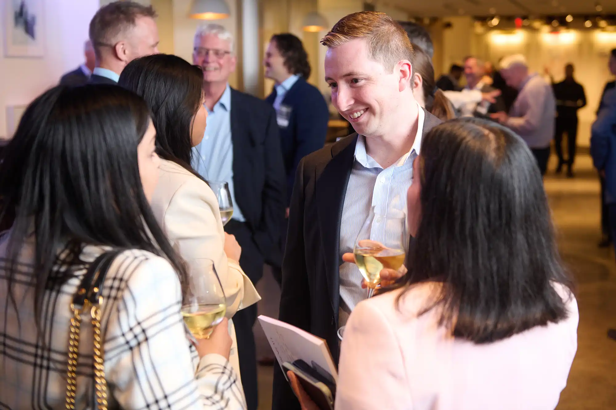 A group of business professionals in suits stand in a circle talking and laughing at a corporate networking reception event.