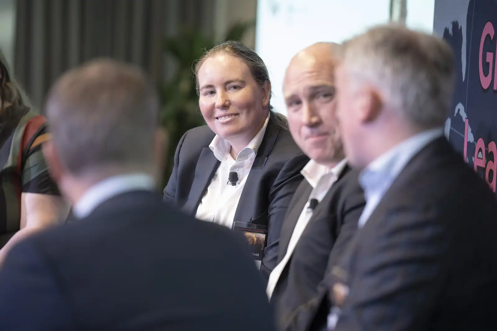 A confident female industry expert smiling while seated on stage alongside male colleagues during an engaging professional corporate panel discussion.