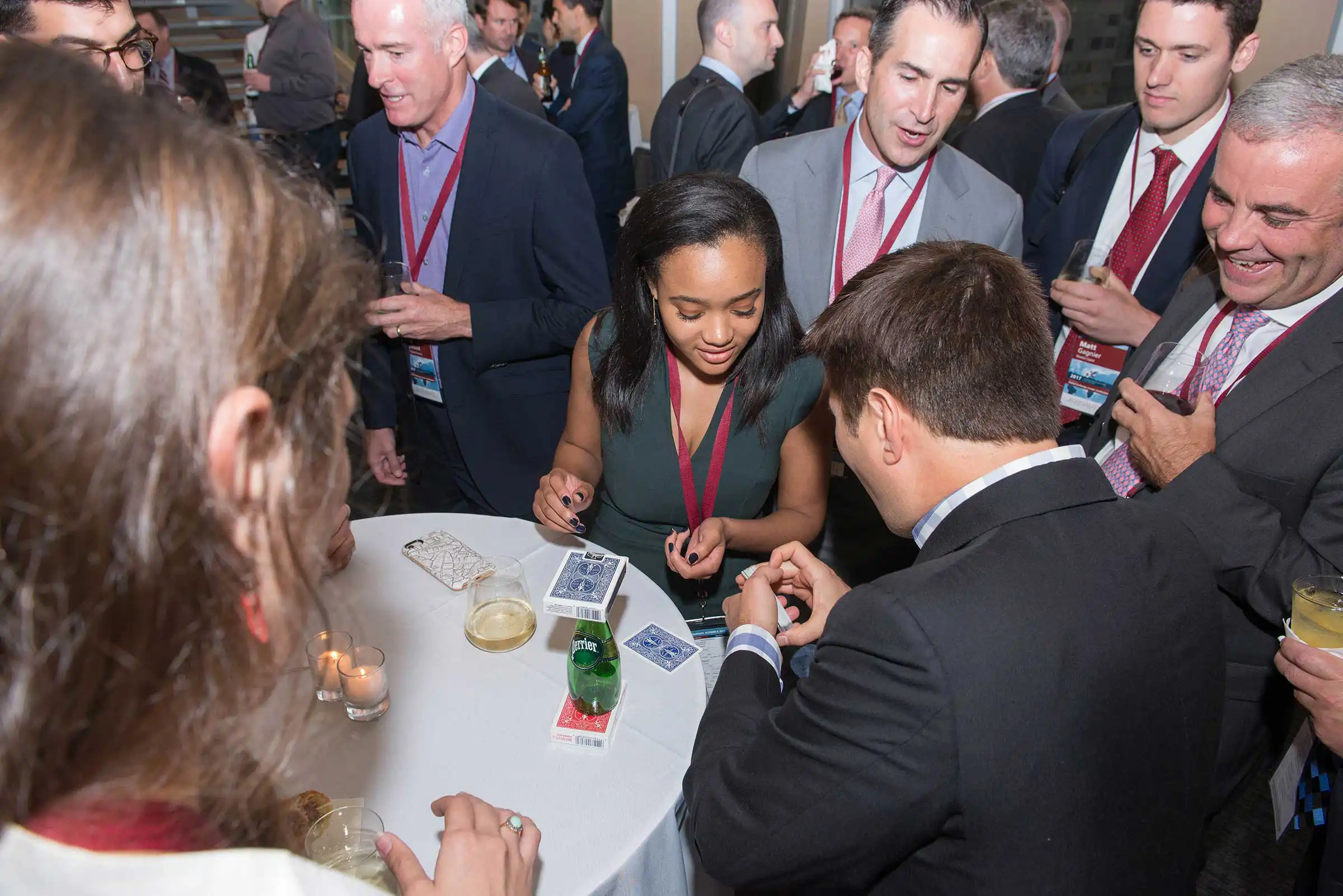 A skilled magician entertains a young woman and male professionals with an impressive card trick at a corporate networking reception.