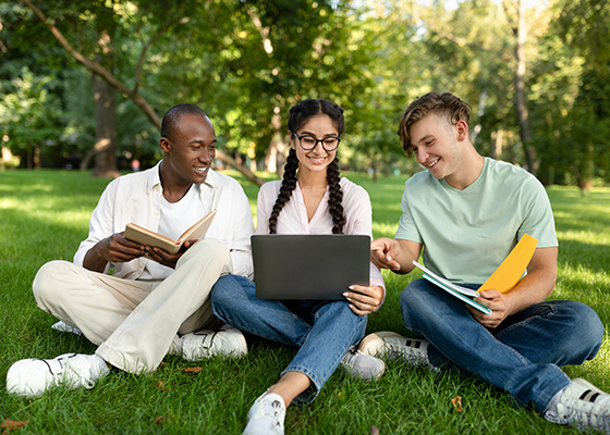 Group of high school students sitting on the grass looking at a laptop and a folder of papers